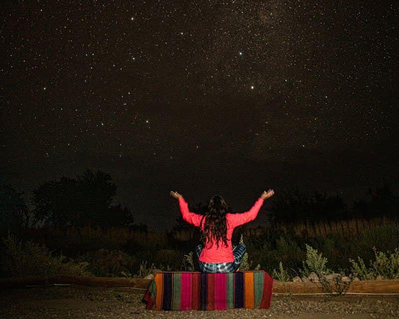 garota de braços abertos observando o céu estrelado