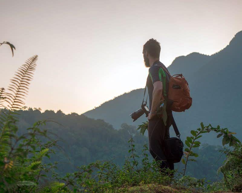 rapaz com câmera com montanhas ao fundo na caminhada da cidade perdida na colômbia