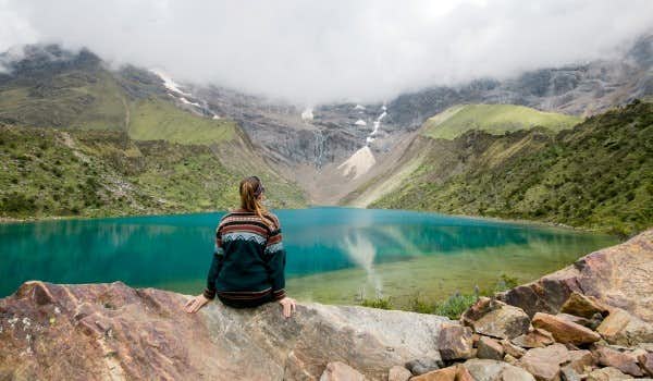 Garota de costas olhando para a lagoa verde no Salkantay sky lodge 4 dias