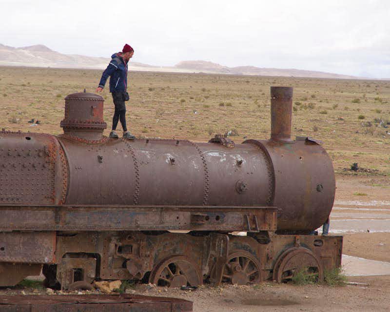 Ein Mann geht mit der Lokomotive eines alten Zuges auf dem Zugfriedhof in der Nähe des Salar de Uyuni