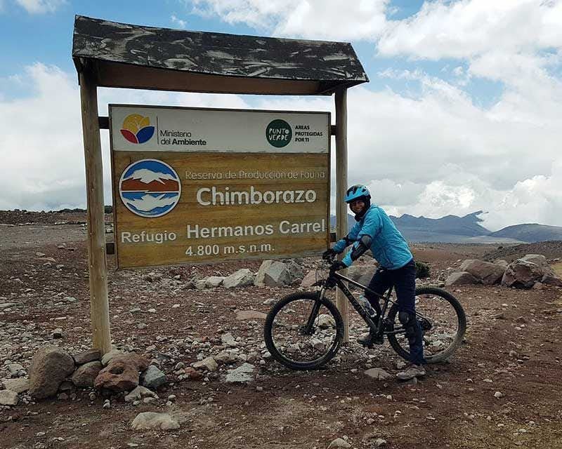 cyclist in front of the sign chimborazo refugio hermanos carrel