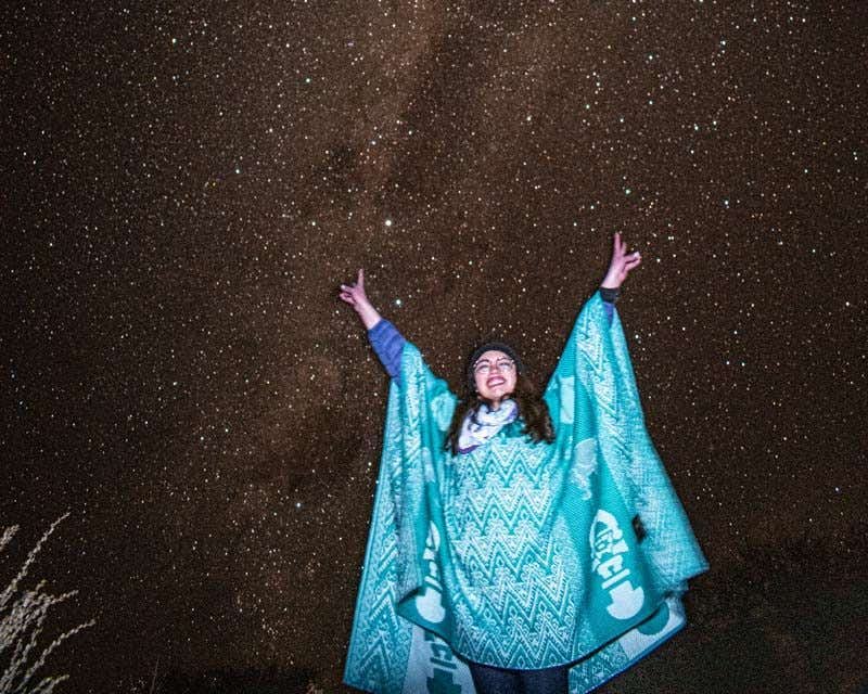 chica feliz con poncho azul posando junto al cielo estrellado