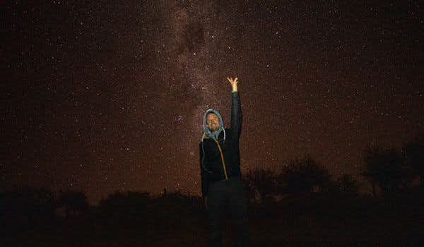 chico con el brazo levantado con el fondo del cielo estrellado