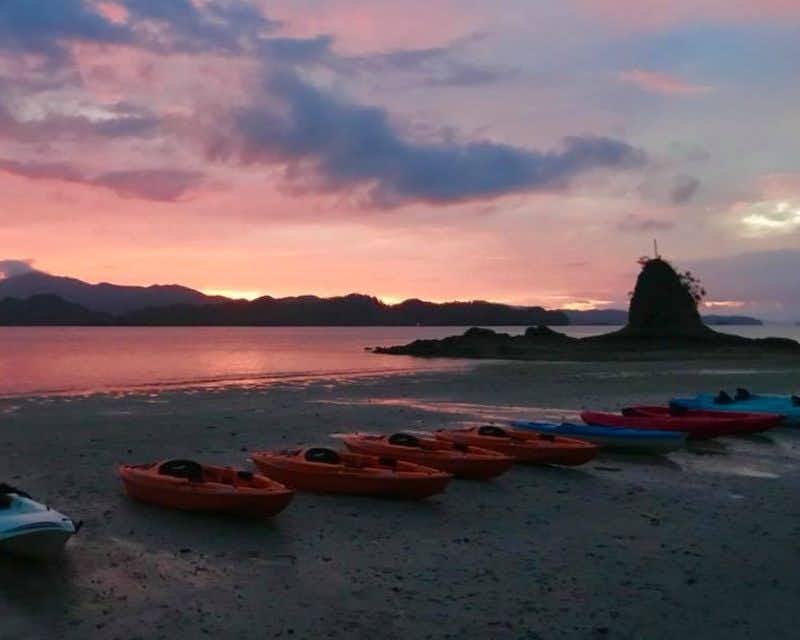 Kayaks sur la plage au coucher du soleil, prêts pour une excursion nocturne en kayak.
