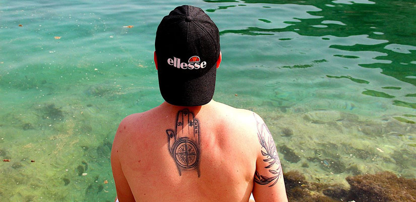 travel tattoo of a compass in a guy back in the water