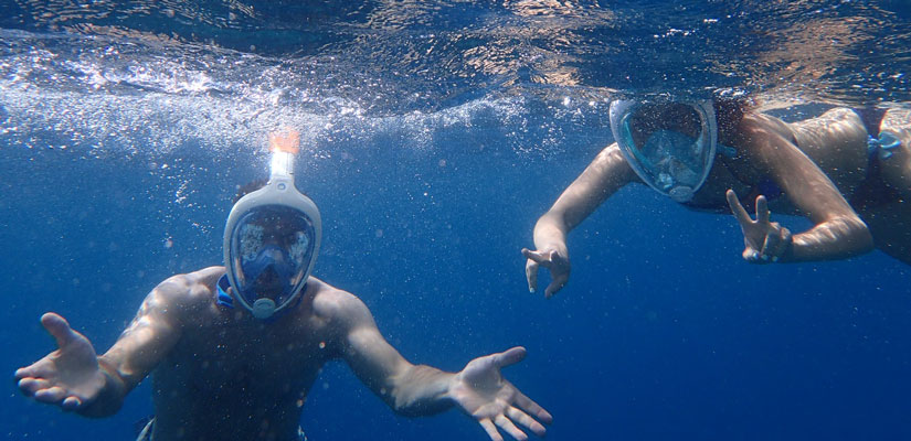 two people snorkeling while signaling to the camera